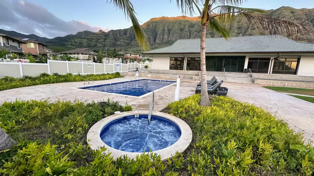 Una piscina al aire libre y una bañera de hidromasaje circular están junto a un edificio de una planta.