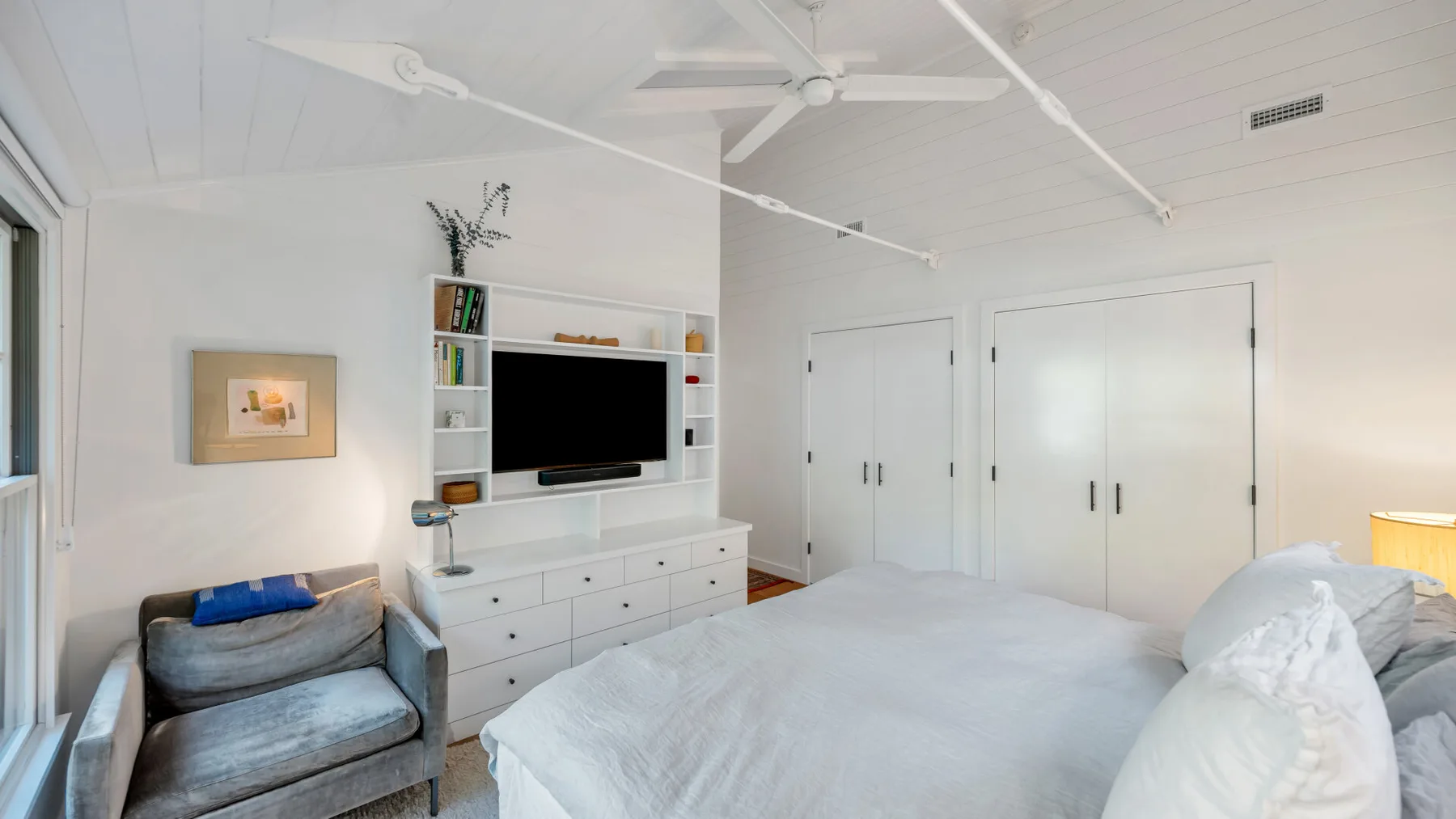 Un dormitorio luminoso con una cama, un televisor y armarios empotrados.