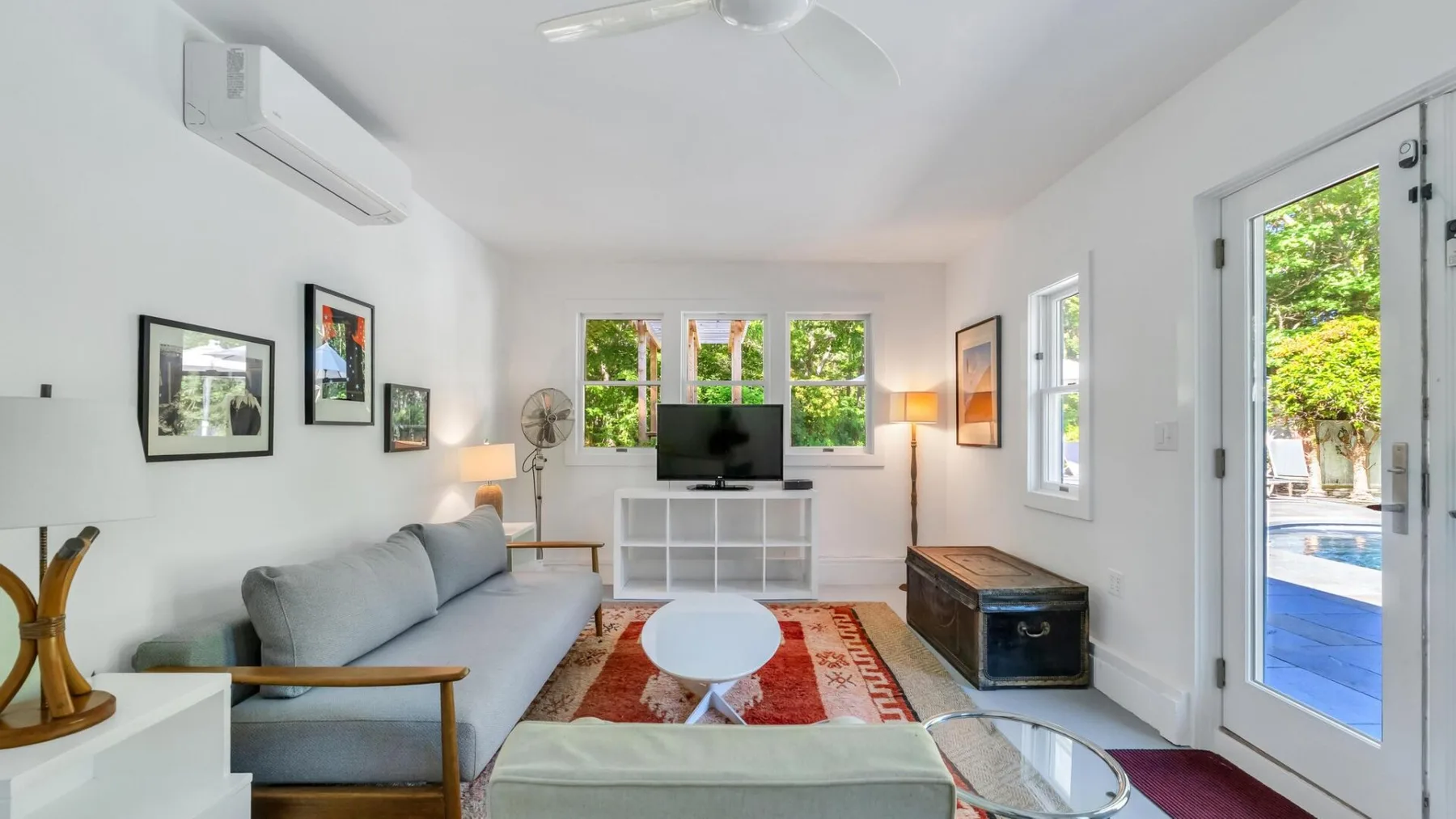 Una sala luminosa con asientos, un televisor y ventanas con vista a una piscina.