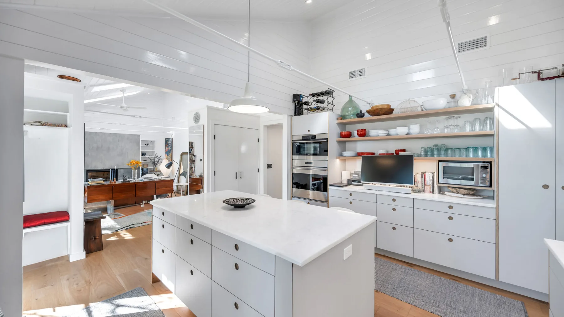 Una cocina blanca y luminosa con una isla central y estantes abiertos.