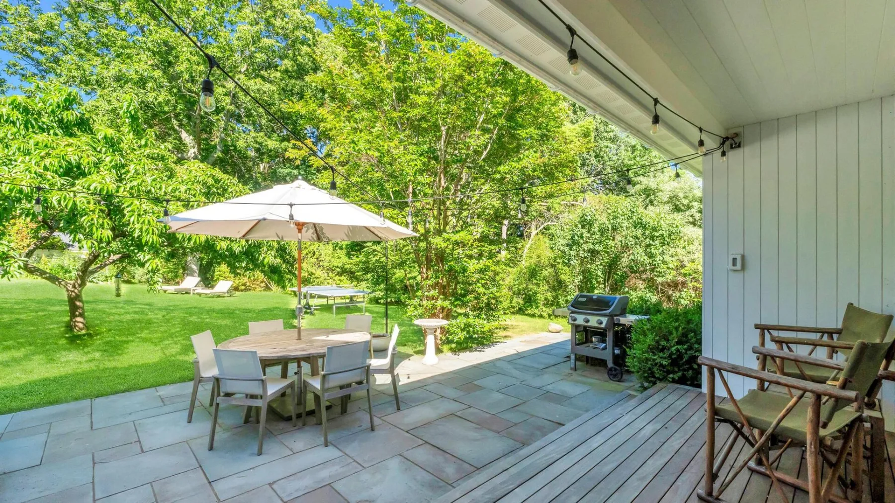 Un patio cubierto con mesa y sillas da a un jardín verde.