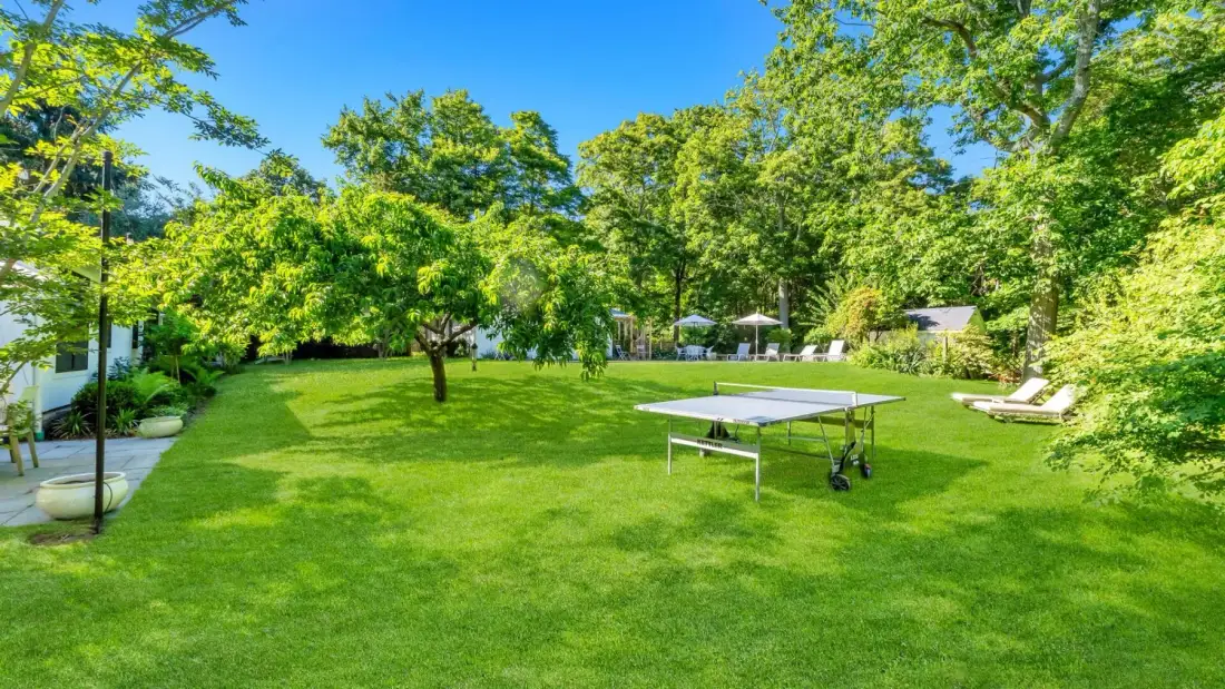 Un jardín frondoso con una mesa de ping-pong y tumbonas sobre el césped.