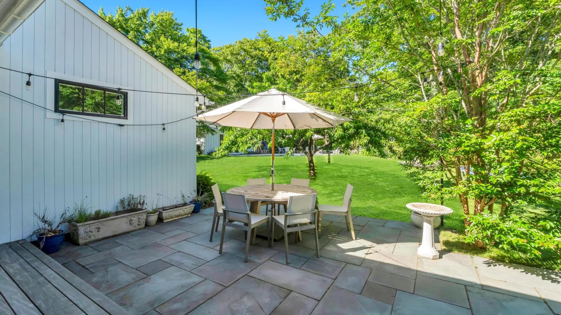 Un patio al aire libre con una mesa de comedor y una sombrilla junto al césped.