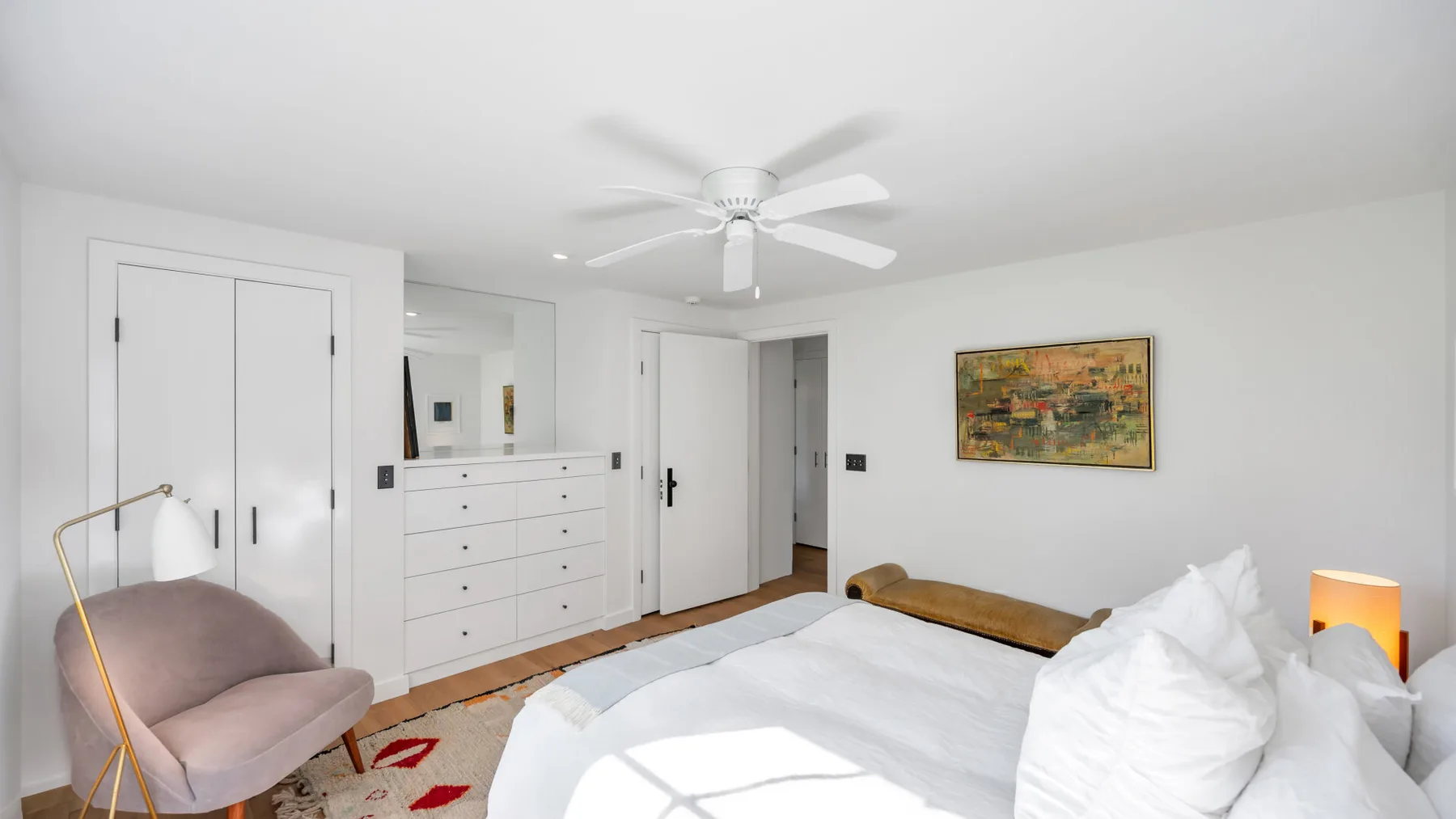 Un dormitorio luminoso con una cama grande, un ventilador de techo y arte en la pared.