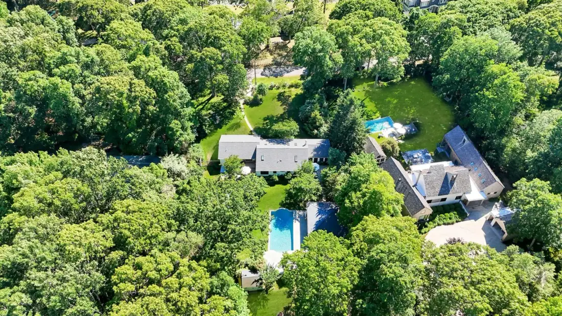 An aerial view shows homes and swimming pools surrounded by dense trees.