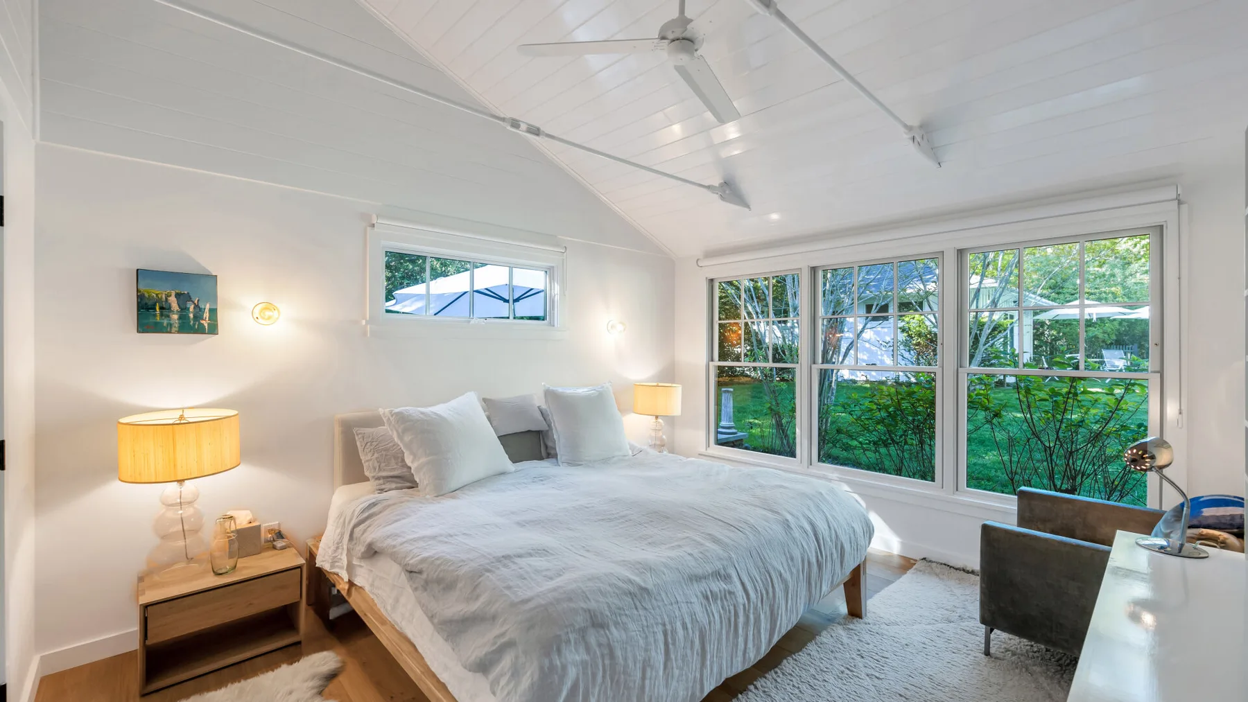 Un dormitorio luminoso con una cama bajo grandes ventanas que dan a la vegetación.