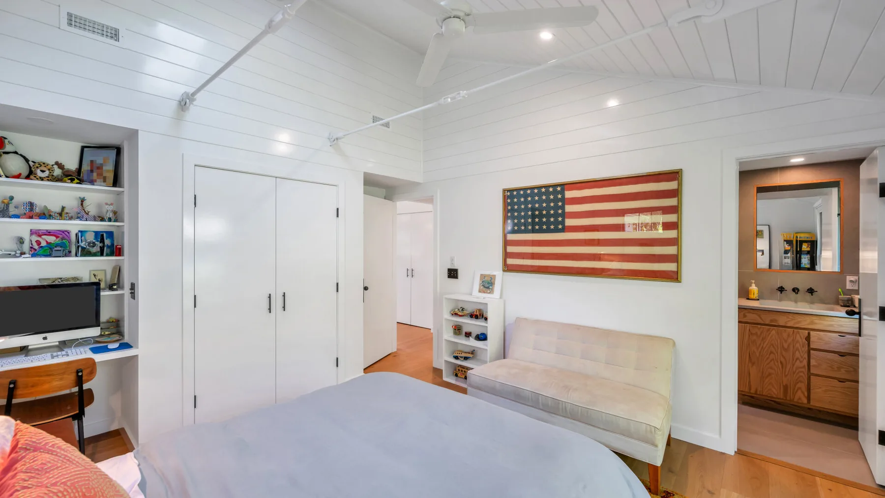 Un dormitorio luminoso con una cama, un pequeño sofá y una bandera estadounidense en la pared.