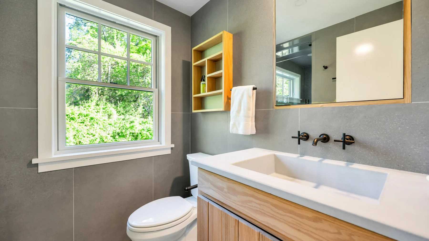 Un baño con un lavabo amplio, espejo de pared y una ventana con vegetación afuera.