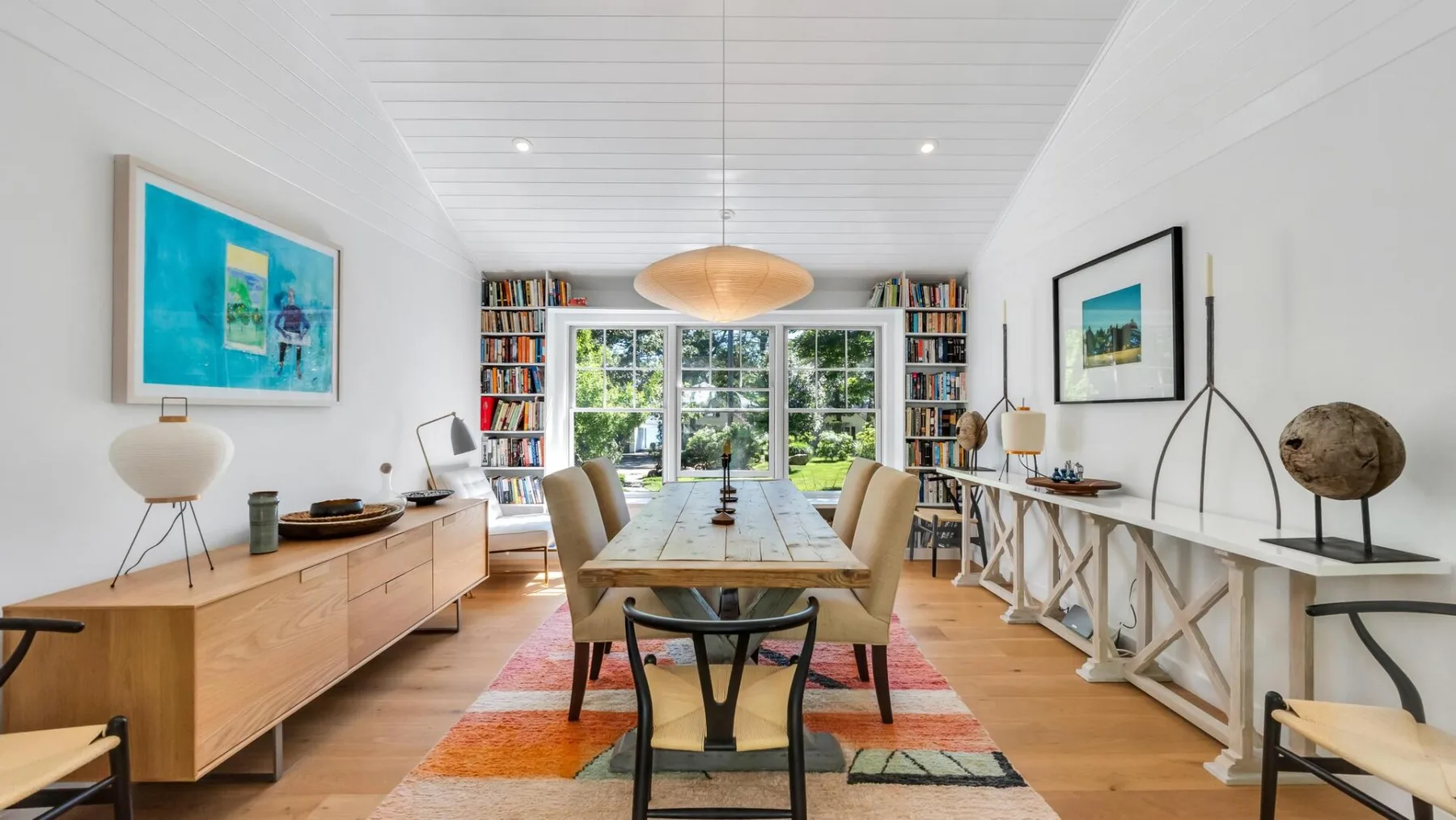 Un comedor luminoso con una mesa larga y estanterías junto a las ventanas.