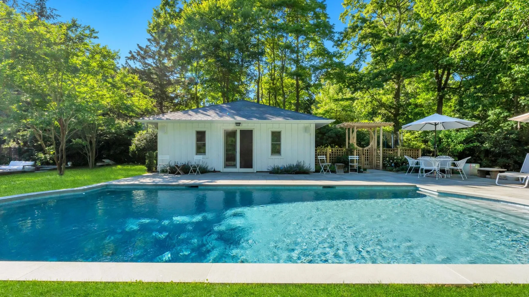Una piscina al aire libre está junto a un pequeño edificio blanco y asientos en el patio.