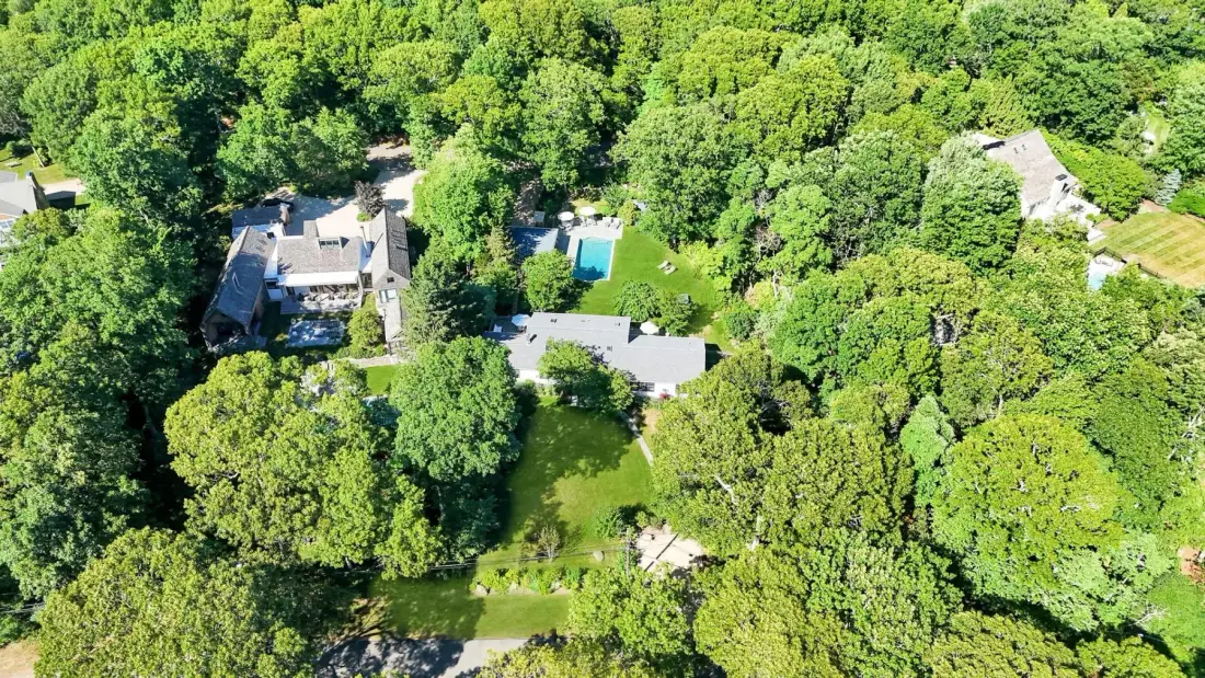 Una vista aérea muestra viviendas, una piscina y bosque circundante.