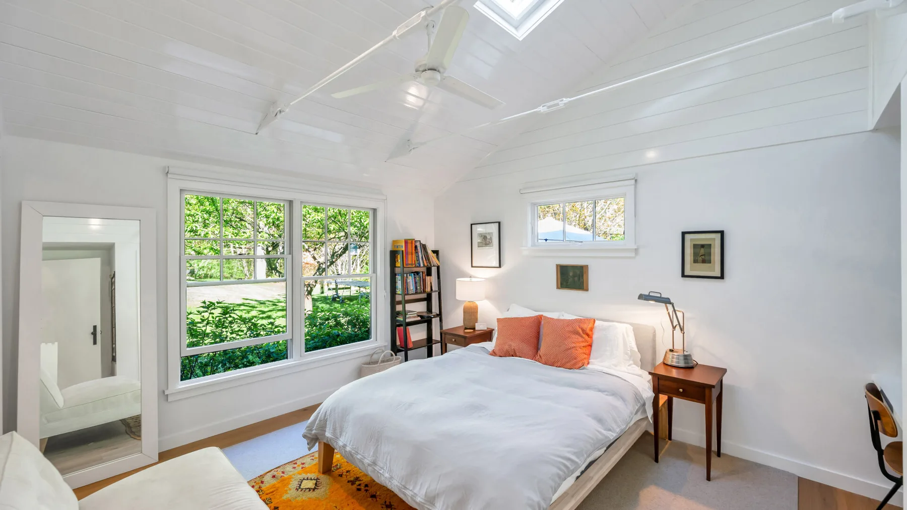Un dormitorio luminoso con cama, ventanas grandes y techo blanco inclinado.