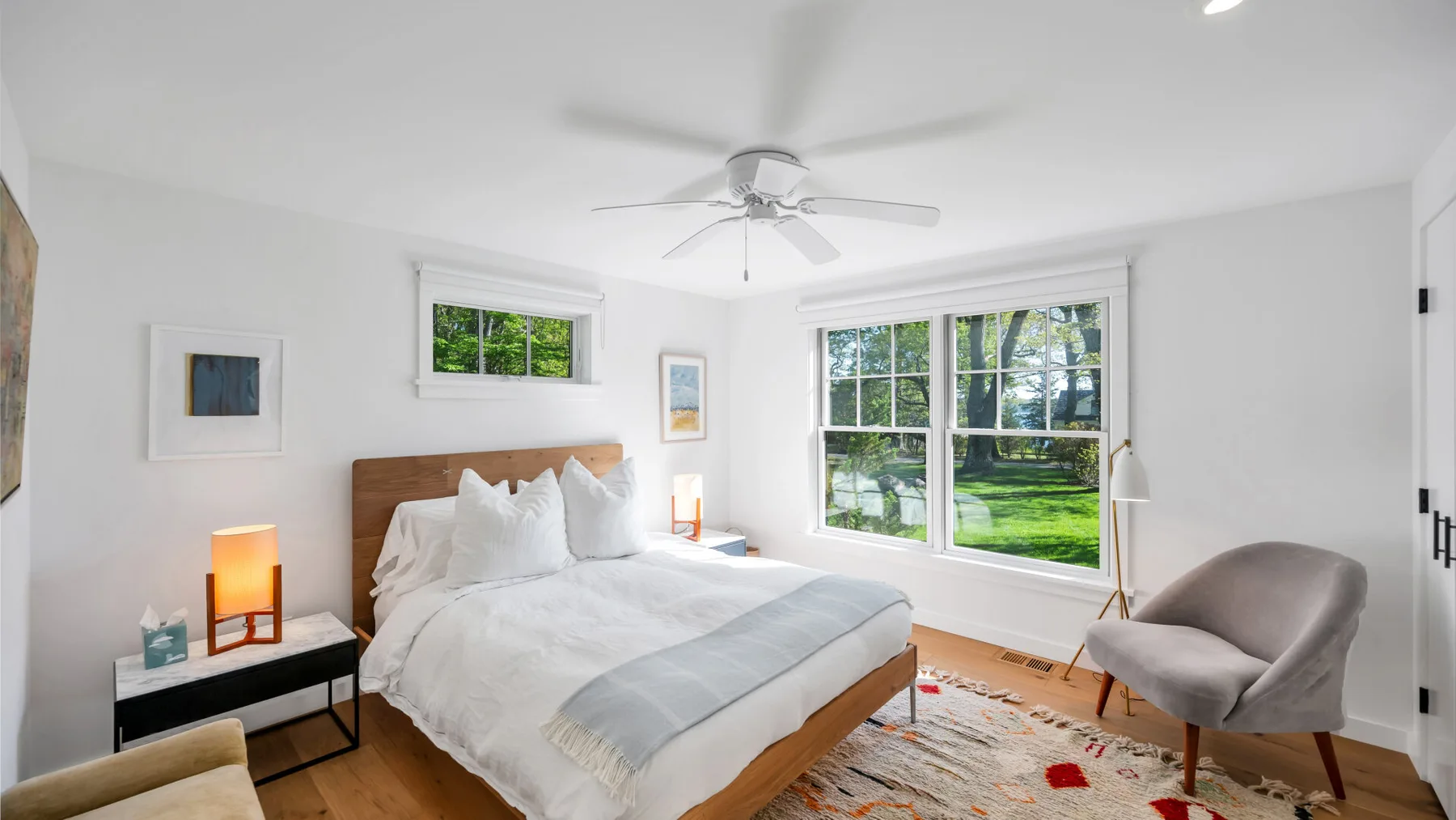 Un dormitorio luminoso con una cama, mesitas de noche y grandes ventanas.