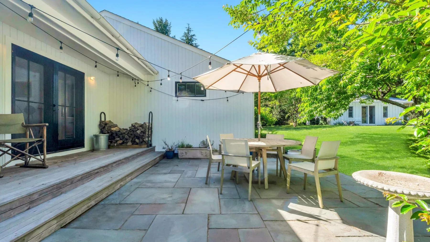Un patio al aire libre con una mesa de comedor y una sombrilla junto a un césped verde.