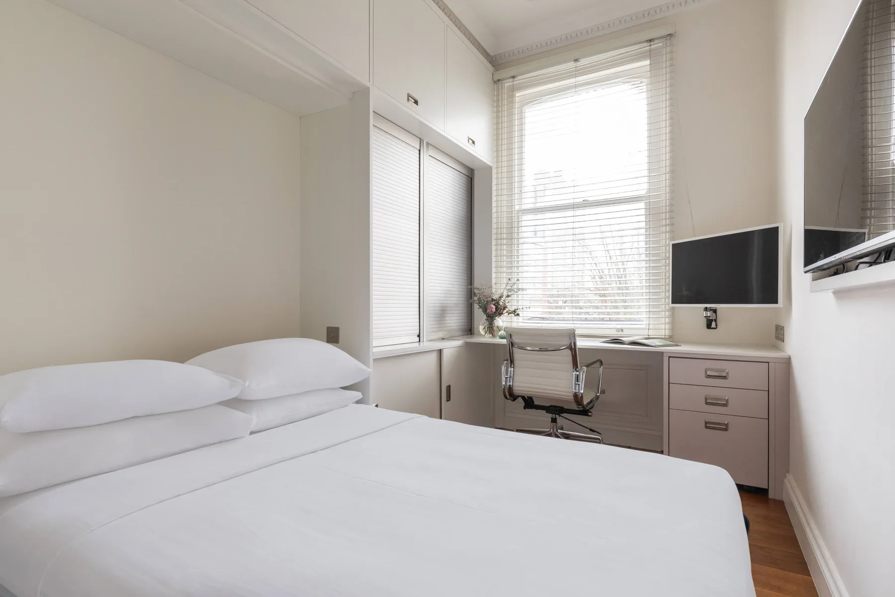 Un dormitorio luminoso con una cama bien hecha y un escritorio junto a la ventana.