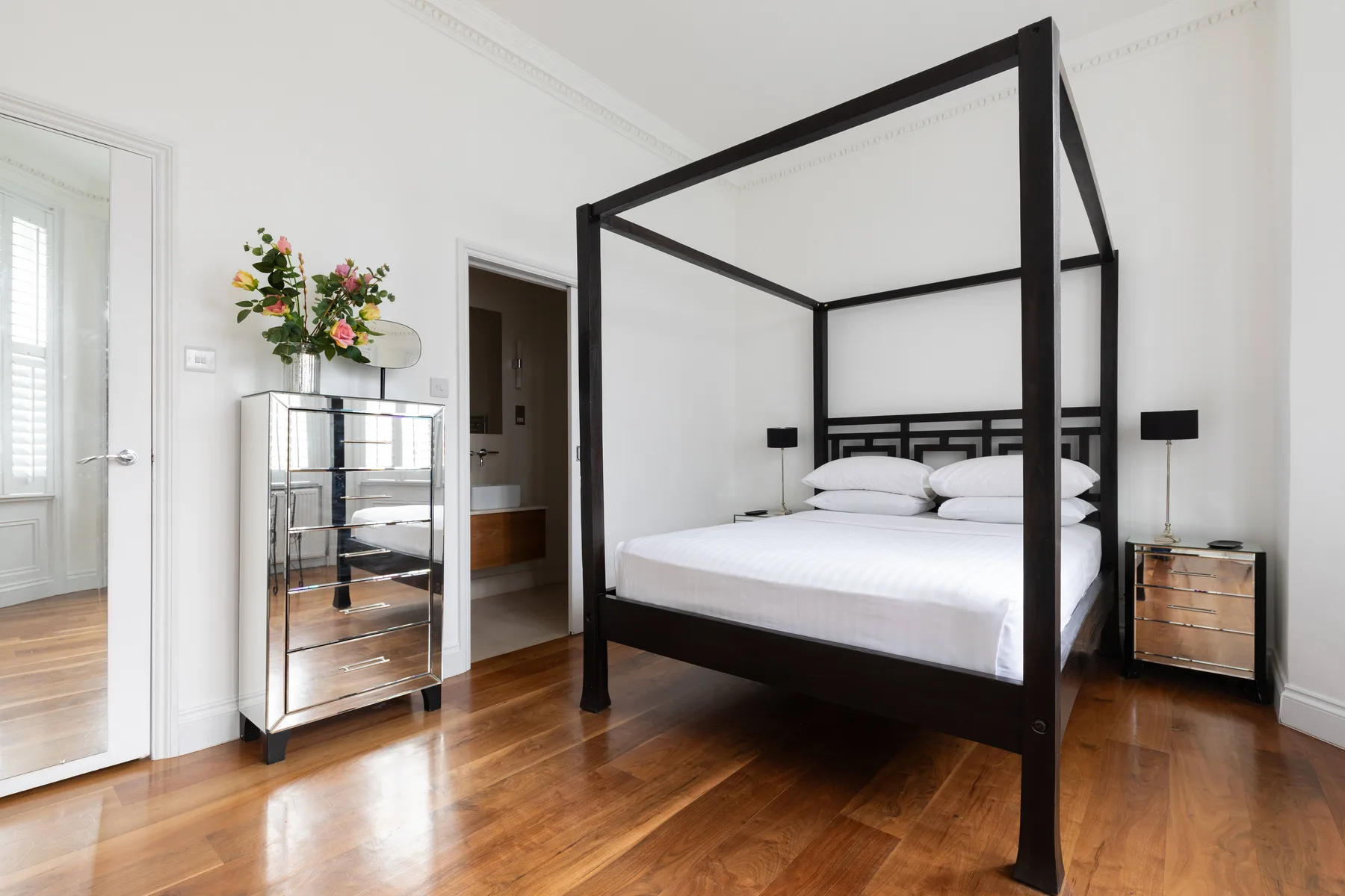 Un dormitorio luminoso con una cama con dosel y suelo de madera pulida.