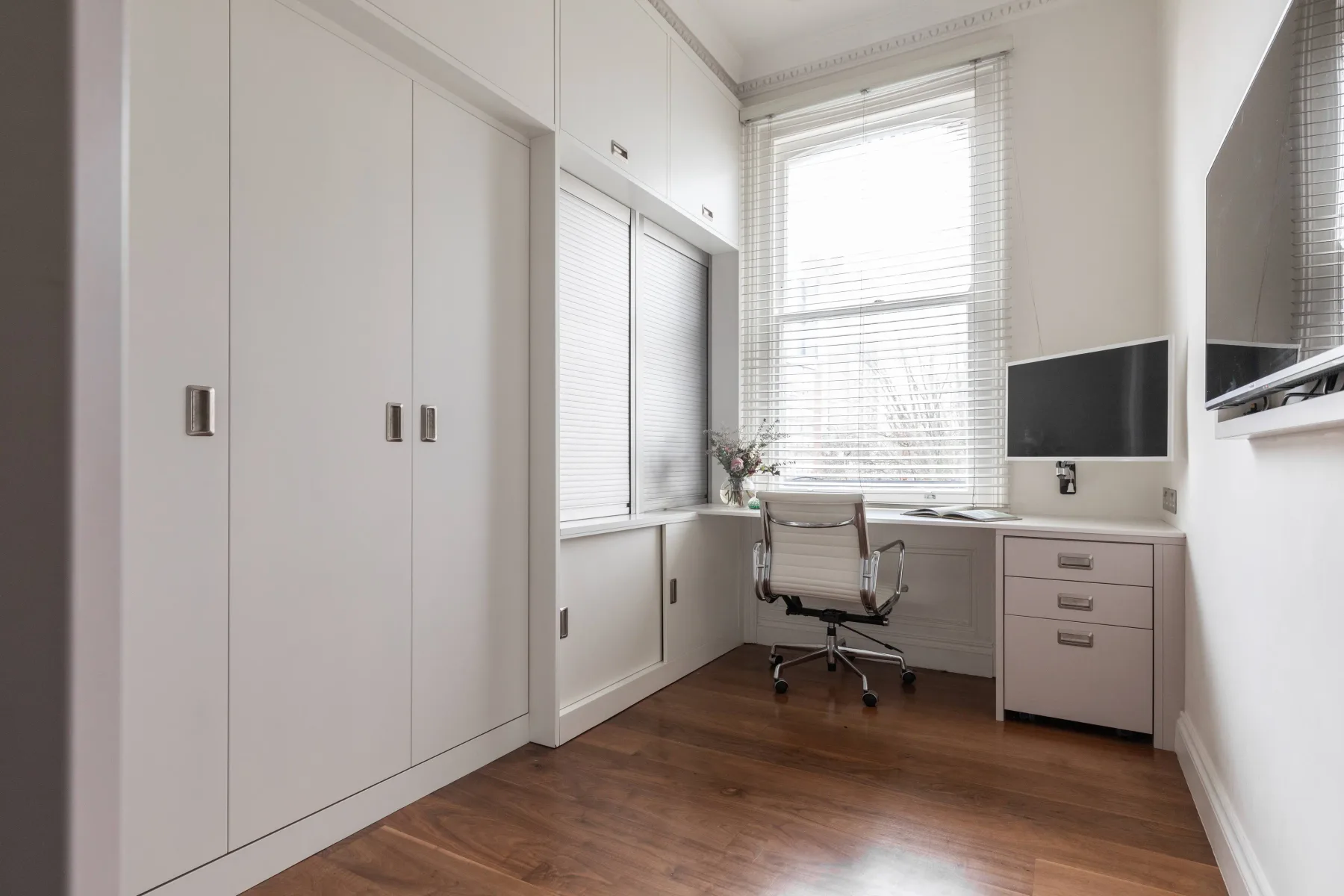 Un espacio de trabajo luminoso en un dormitorio, con escritorio, silla y ventanas grandes.