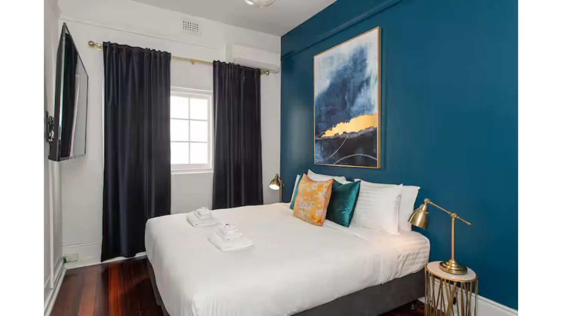 A bedroom with a neatly made bed, dark curtains, and a blue accent wall.