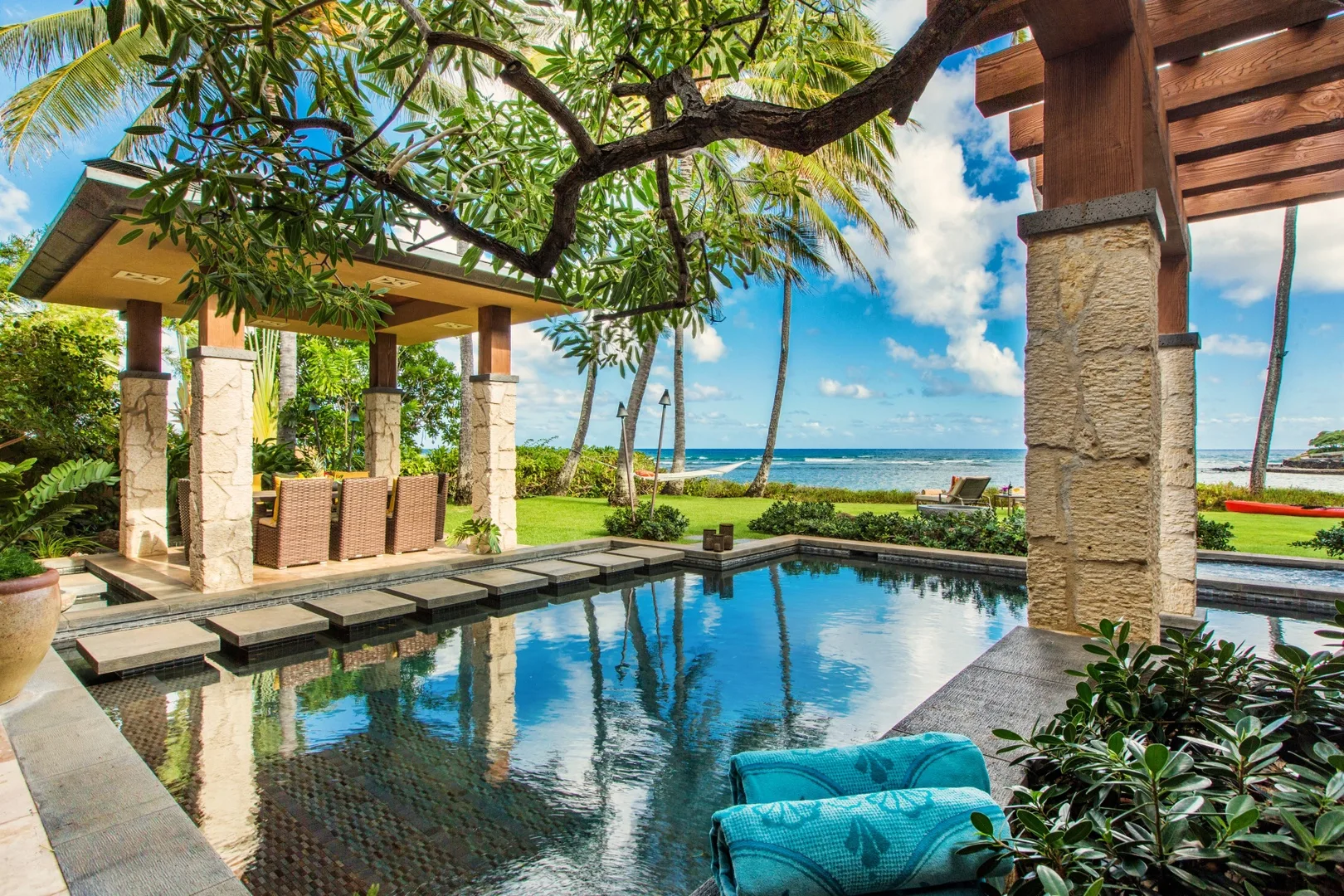 Una piscina tropical al aire libre refleja los árboles junto a una zona de asientos cubierta.