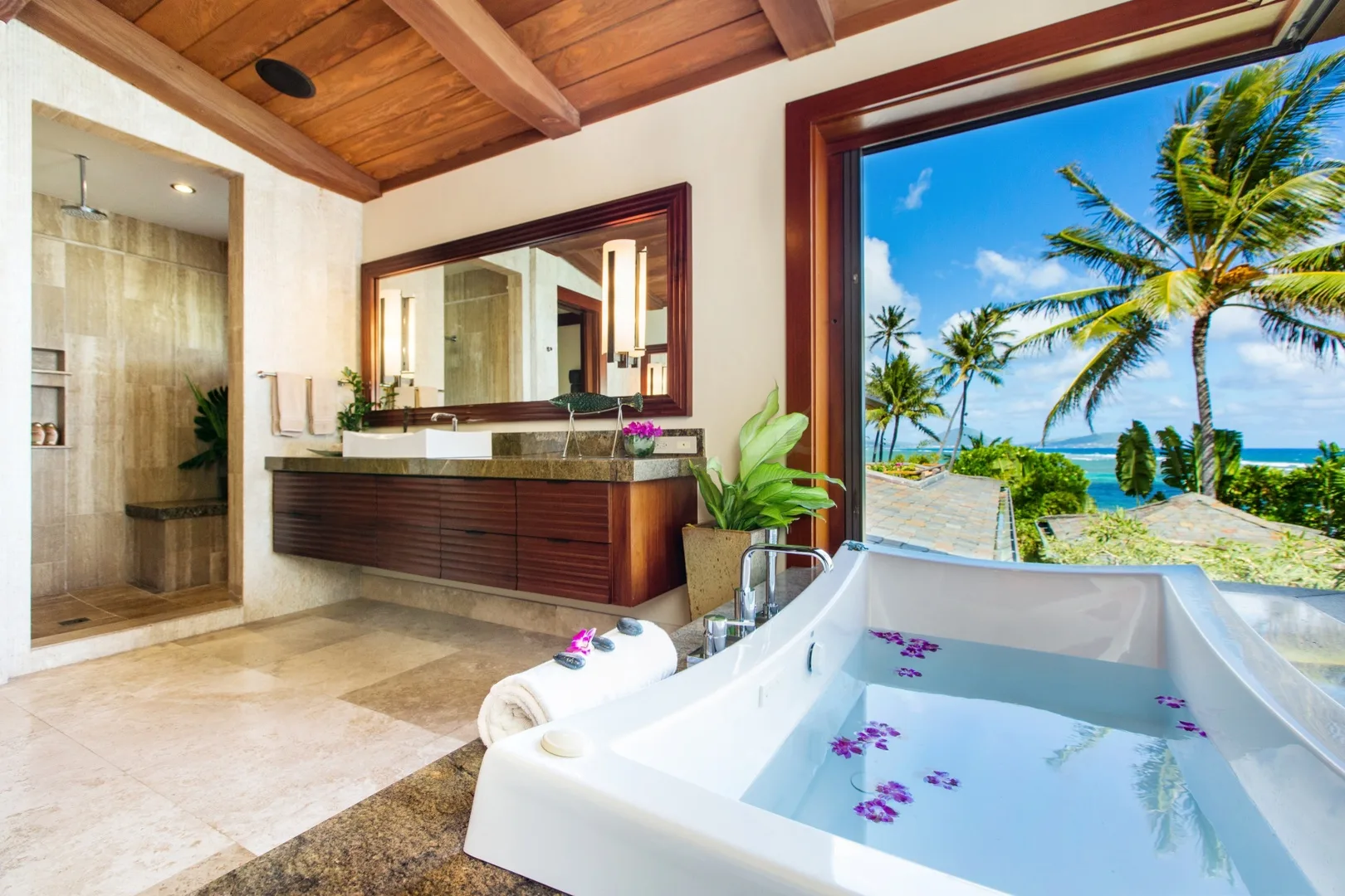 Un baño con una bañera junto a una ventana amplia con vistas a palmeras y al mar.