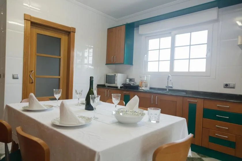 Una mesa está preparada en una cocina luminosa con gabinetes color turquesa y madera.