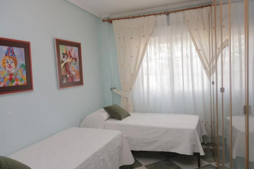 Un dormitorio con dos camas junto a una gran ventana con cortinas translúcidas.