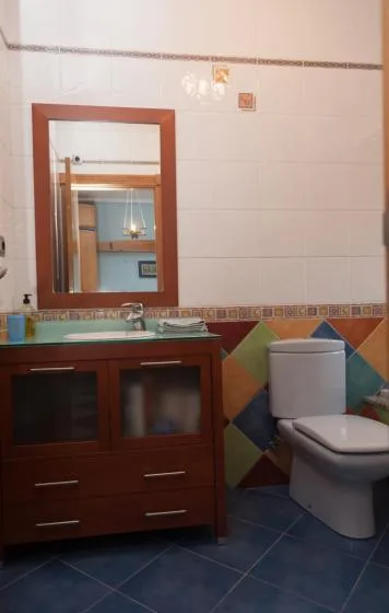 Un baño alicatado con lavabo, espejo de pared e inodoro.