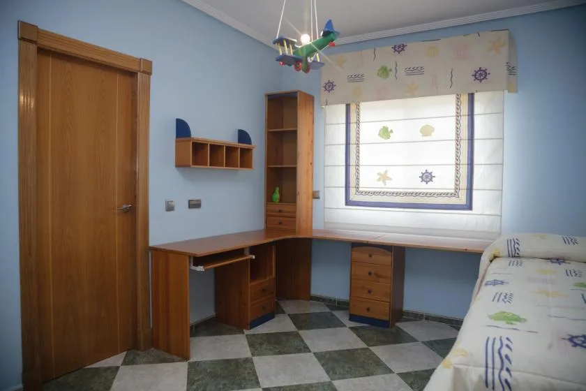 Un dormitorio con un escritorio de madera bajo una ventana y una cama al lado.