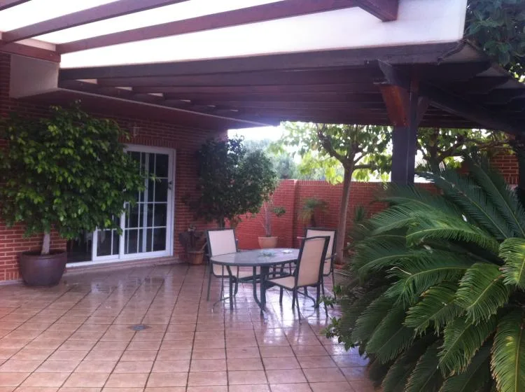 Un patio cubierto con una mesa de vidrio, asientos y plantas frondosas.
