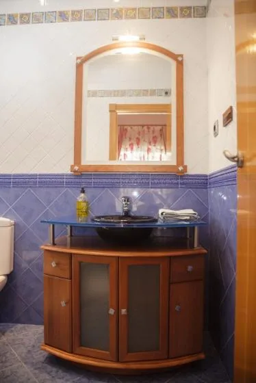Un tocador de baño con lavabo y espejo frente a paredes revestidas de azulejos.