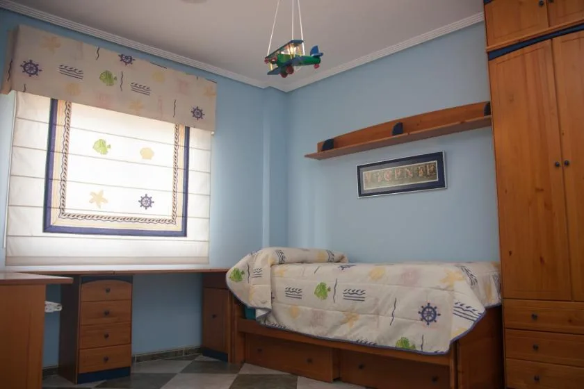Un dormitorio con una cama individual, muebles de madera y una cortina estampada.