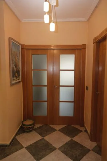 Un pasillo de tonos cálidos con puertas dobles de madera y suelo de baldosas a cuadros.