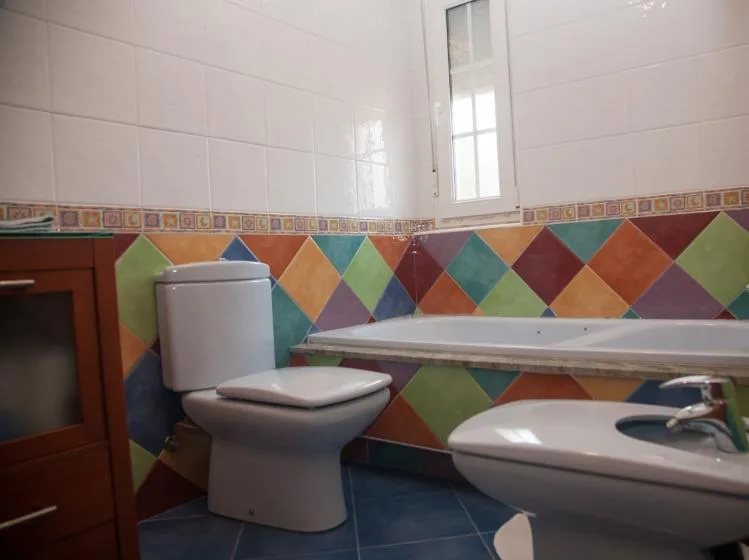 Un baño con bañera, inodoro y lavabo junto a paredes de azulejos coloridos.