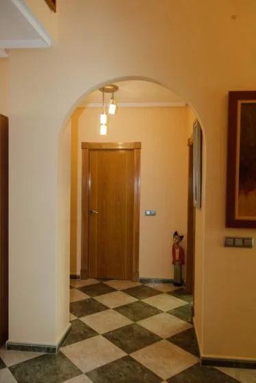 Un pasillo con arco, una puerta de madera y un suelo de baldosas a cuadros.