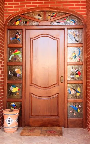 Una puerta de entrada de madera decorada con paneles de vidrio colorido en una pared de ladrillo.