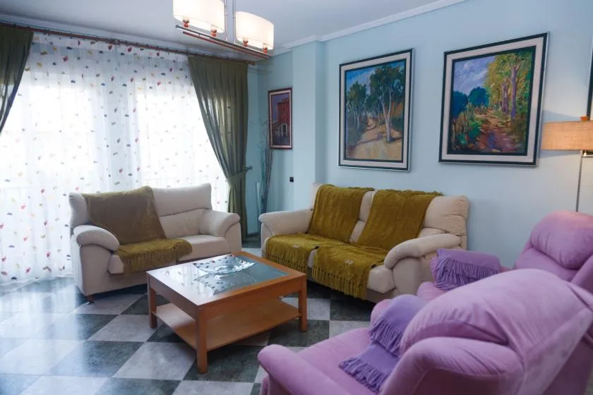 Una sala de estar con asientos, una mesa de centro y cuadros de paisajes.