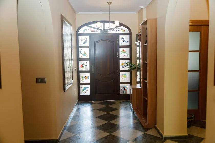 Una entrada con una puerta oscura, paneles de vidrio decorativos y piso de baldosas.