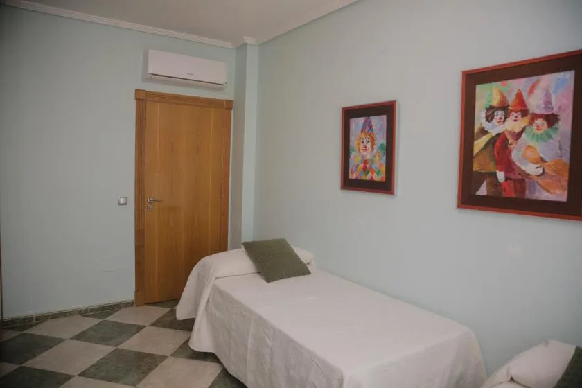 Un dormitorio con una cama individual, una puerta de madera y cuadros en las paredes.