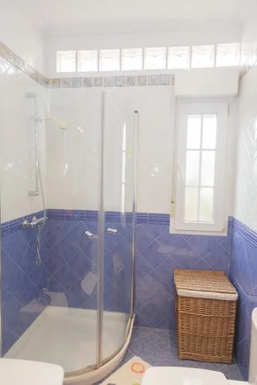 Un baño con azulejos, una ducha de vidrio y una cesta de mimbre.