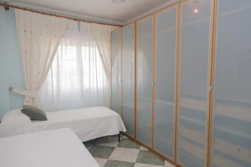Un dormitorio con dos camas junto a una ventana con cortinas y armarios empotrados.