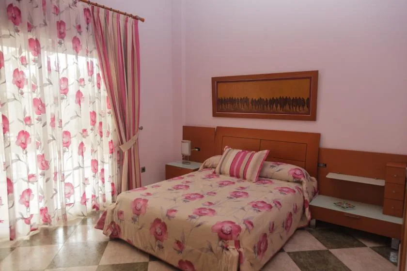Un dormitorio con una cama vestida con ropa floral junto a una ventana con cortinas.