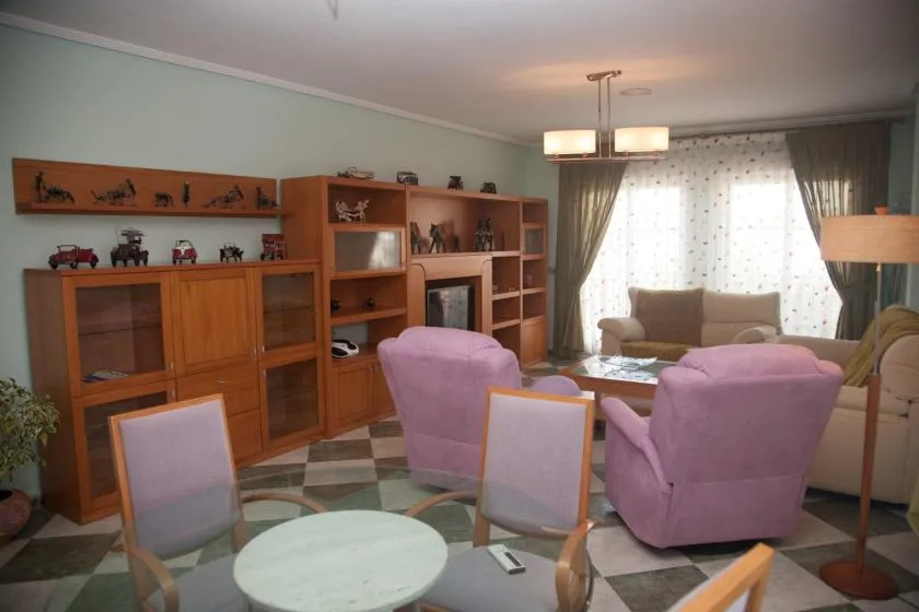 Sala de estar con asientos rosas, estanterías de madera y una ventana luminosa con cortinas.