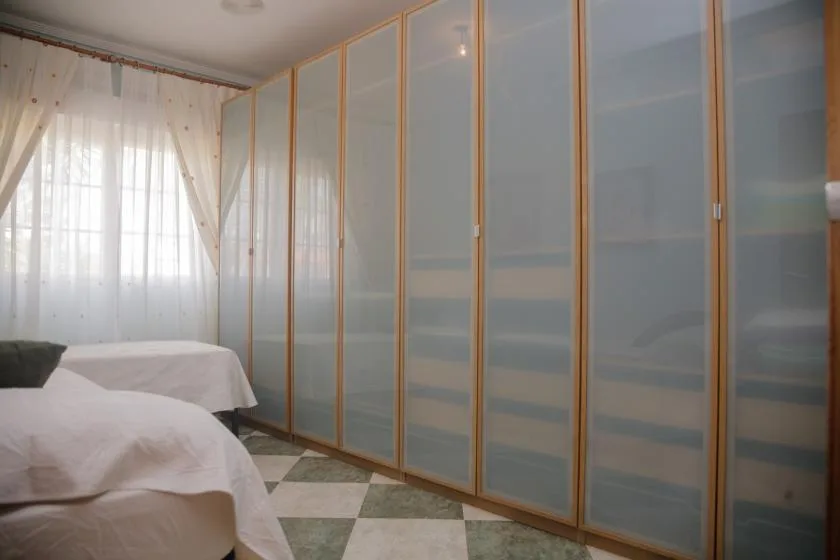 Dormitorio con camas junto a una larga fila de puertas correderas translúcidas de armario.