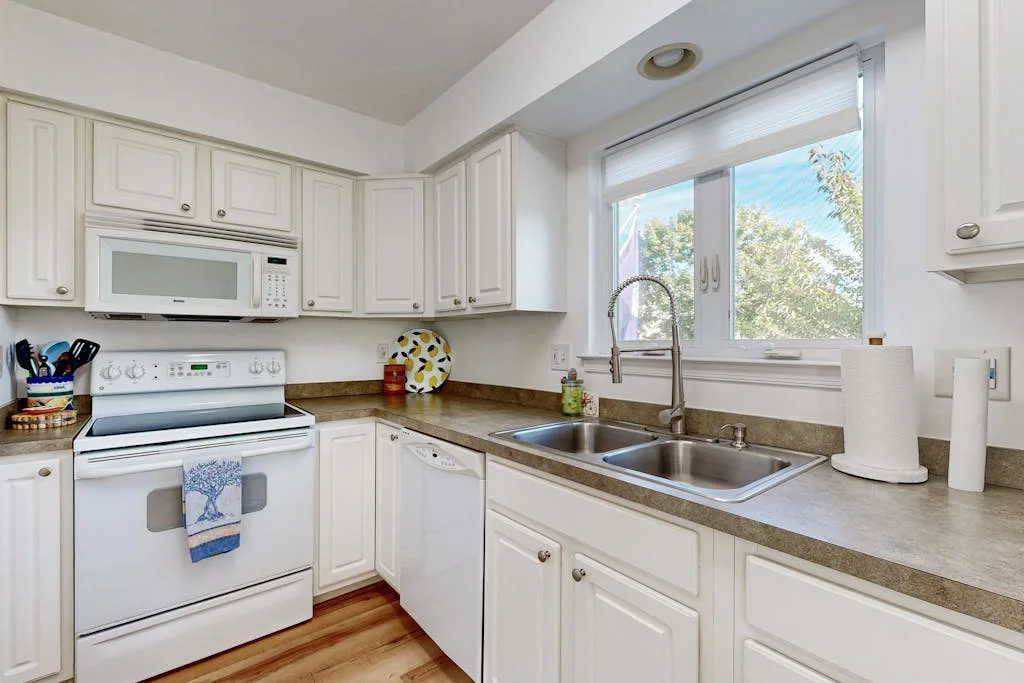 A bright kitchen with white cabinets, a stove, and a sink beneath a window.
