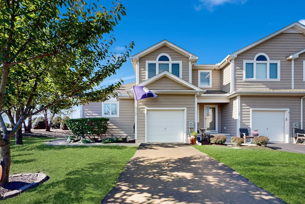 A row of attached homes with garages faces a paved driveway and green lawn.