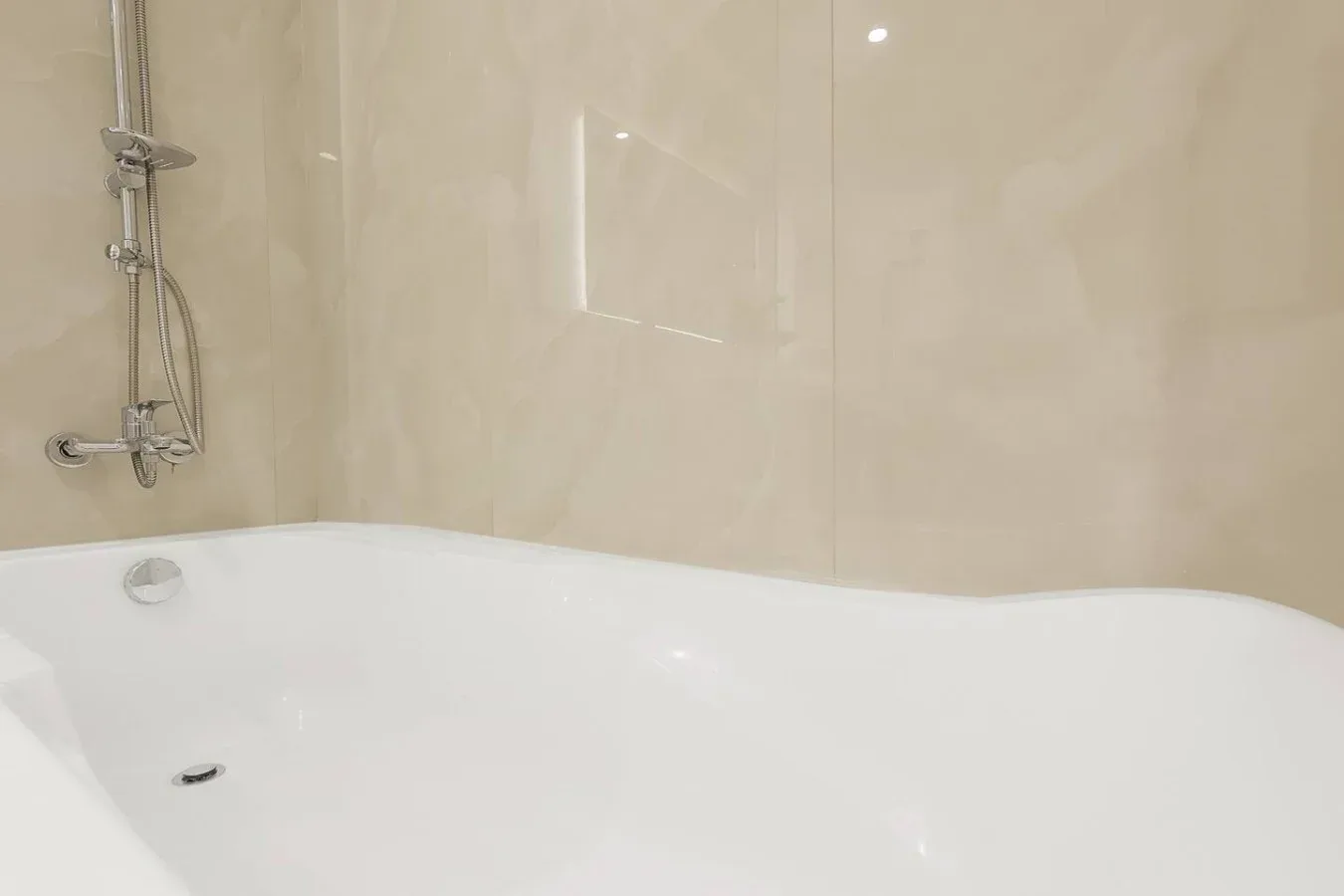 A bathtub with a wall-mounted shower fixture sits against light-colored tiled walls.