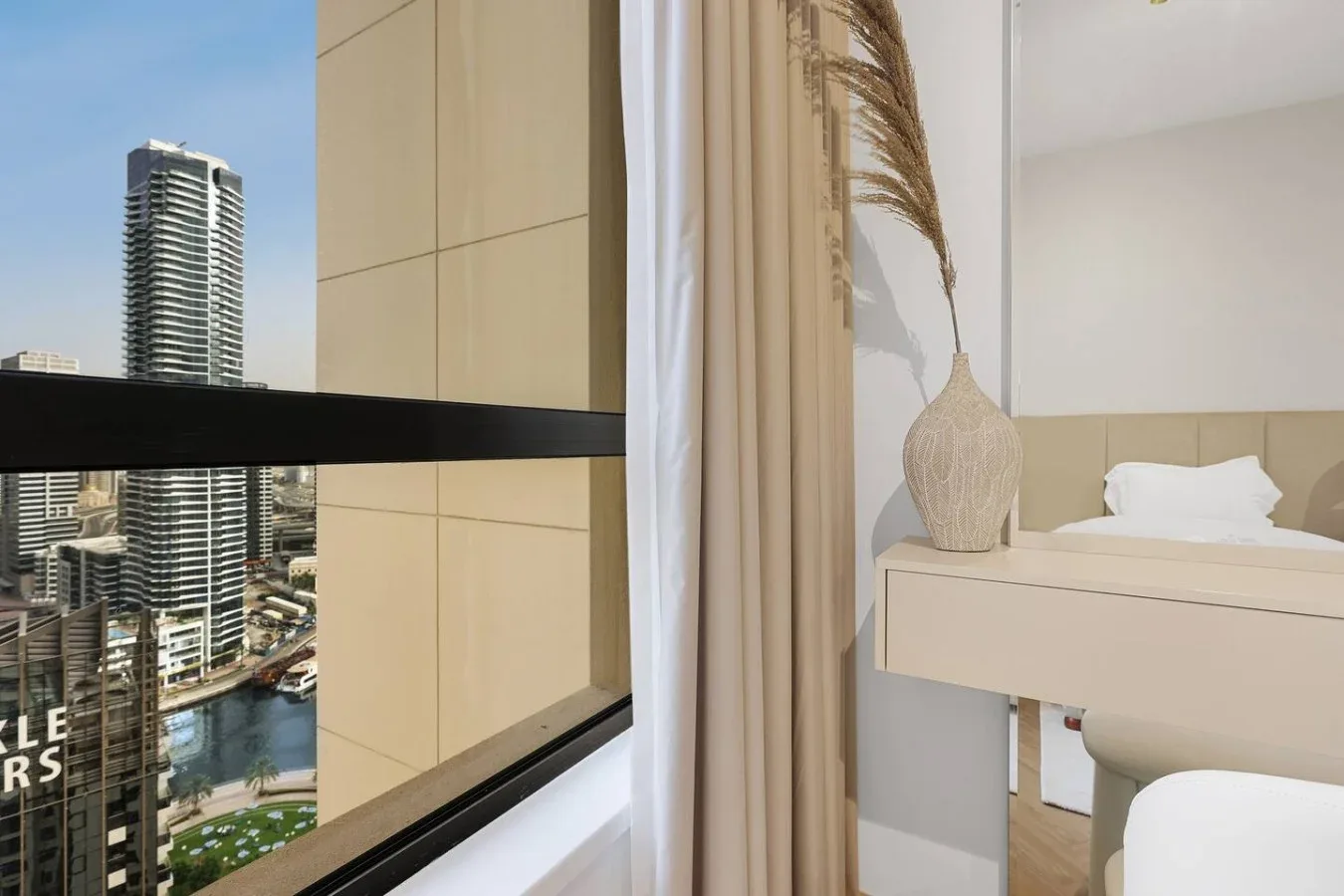 A bedroom with a bed beside a window overlooking nearby high-rise buildings.