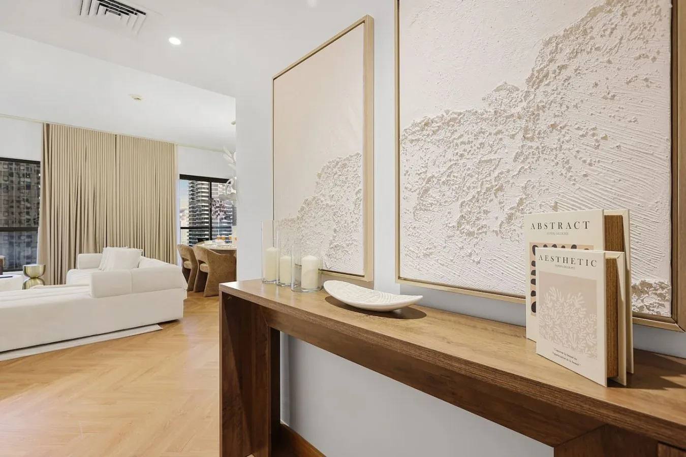 A living room with white seating and framed abstract artwork above a wooden console.
