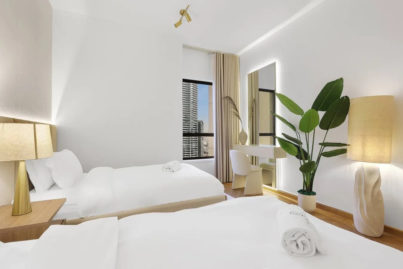 A bright bedroom with white bedding, a small desk, and a leafy plant.