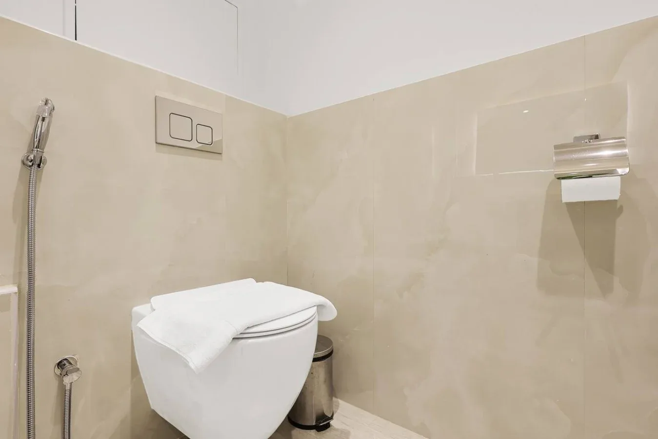 A tiled bathroom with a toilet, handheld shower, and wall-mounted dispenser.